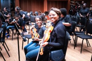 mom and daughter smile for a photo with their violins